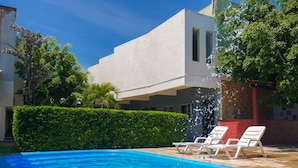 A swimming pool with clear blue water, surrounded by a white building, a hedge, and a tree. - Marbello Ariaú Hotel (Fortaleza)
