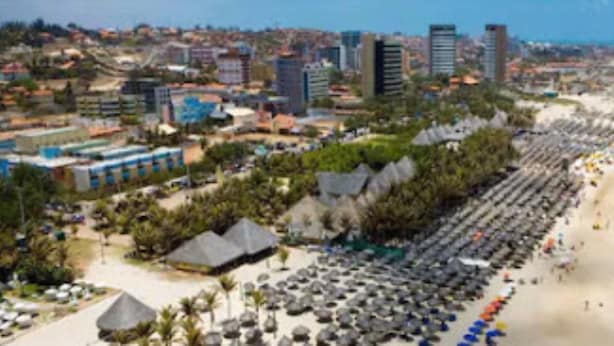 A coastal cityscape with a beach lined with umbrellas and beach chairs. - Marbello Ariaú Hotel (Fortaleza)