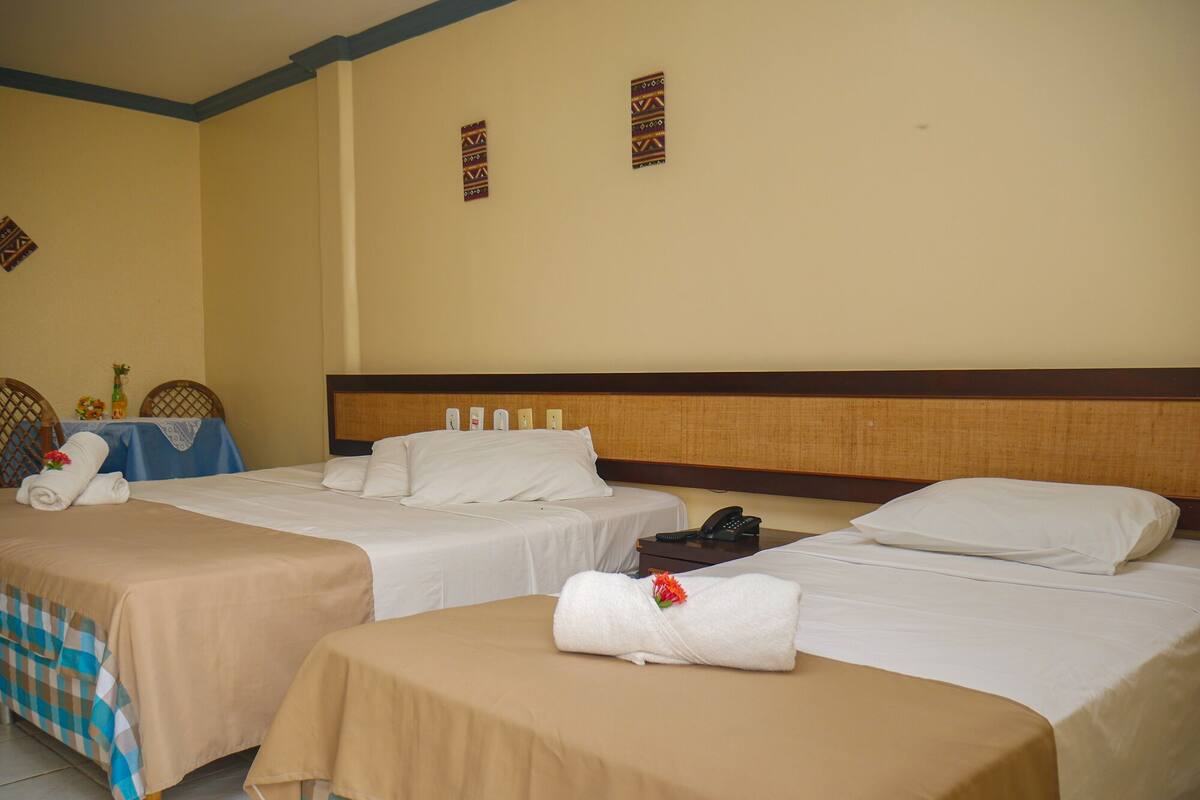Ein Hotelzimmer mit drei Betten, einem kleinen Tisch mit einer Vase und einem Telefon auf einem Nachttisch.