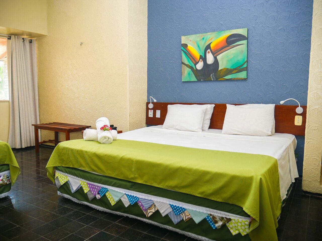 Habitación de hotel con una cama grande, cubrecama verde y un cuadro colorido en la pared.