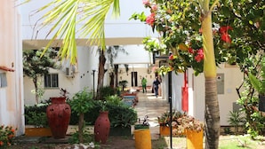 A courtyard with a pathway leading to a building, surrounded by potted plants and a large red vase. - Marbello Ariaú Hotel (Fortaleza)