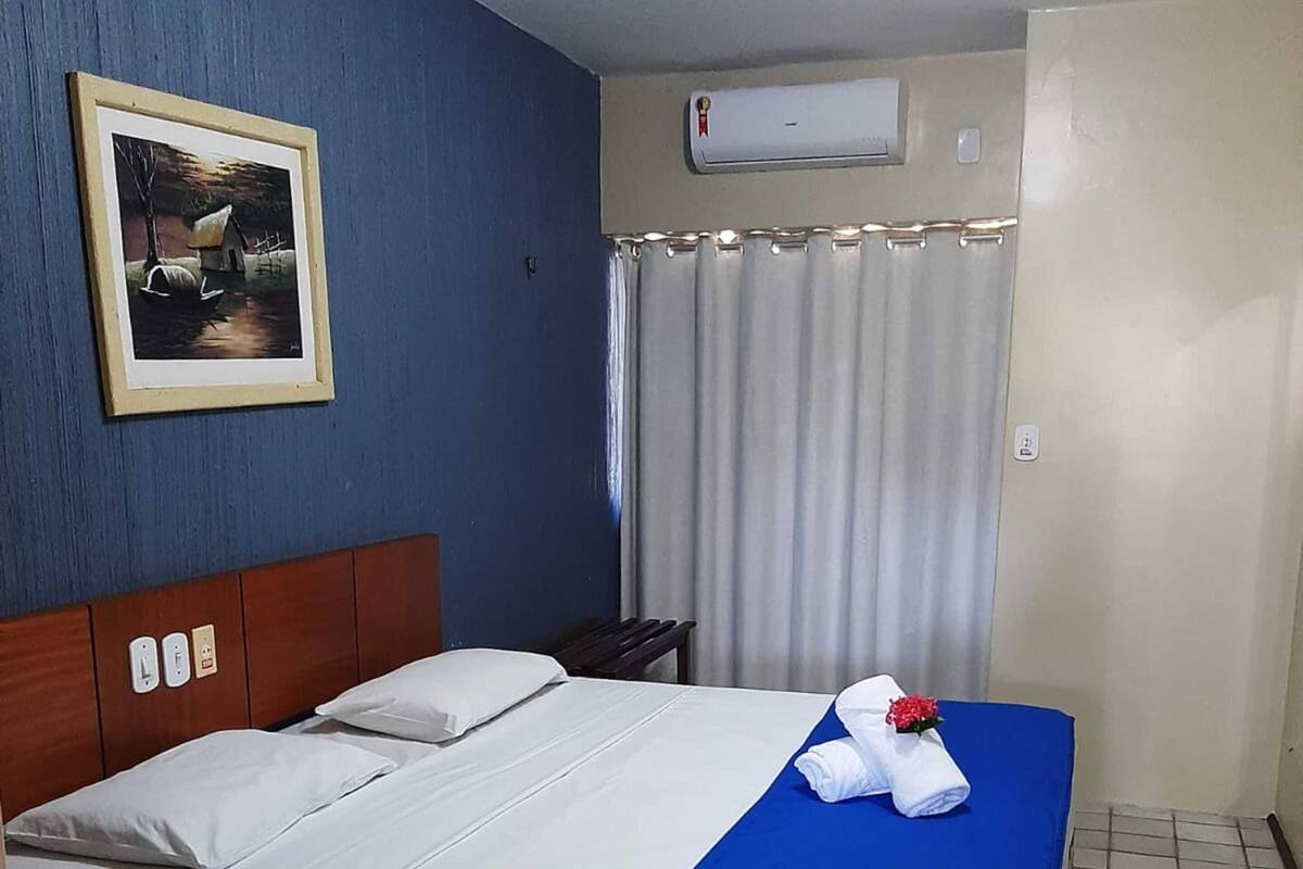 Ein Hotelzimmer mit Bett, einem Bild an der Wand, einer Klimaanlage und einem Vorhang.