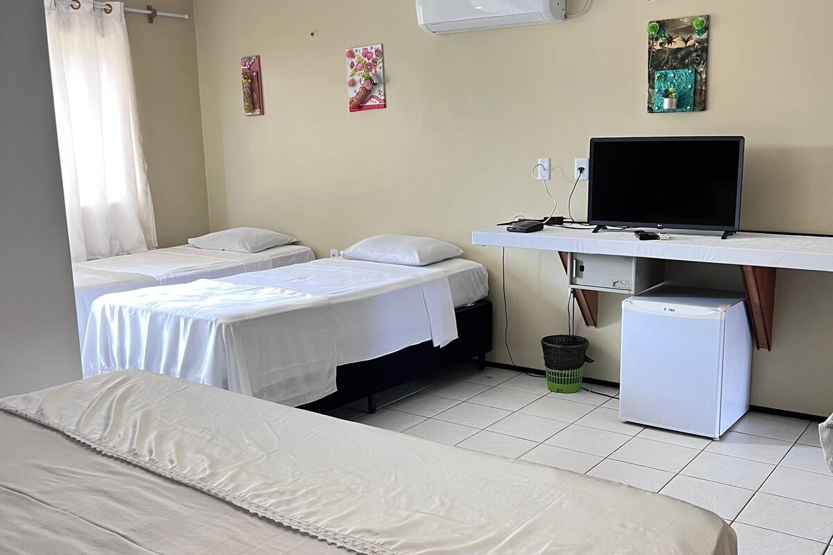 Ein Hotelzimmer mit zwei Betten, einem Schreibtisch mit Computer, einem Kühlschrank und einer Wandklimaanlage.
