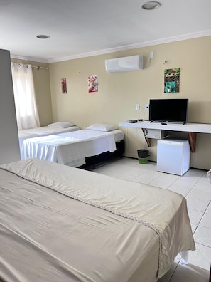 Ett hotellrum med två sängar, ett skrivbord med en dator, ett kylskåp och ett fönster med gardiner.