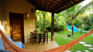 A hammock, a wooden door, a table with chairs, and a pool in a garden. - Brasil Tropical Village (Tibau do Sul)