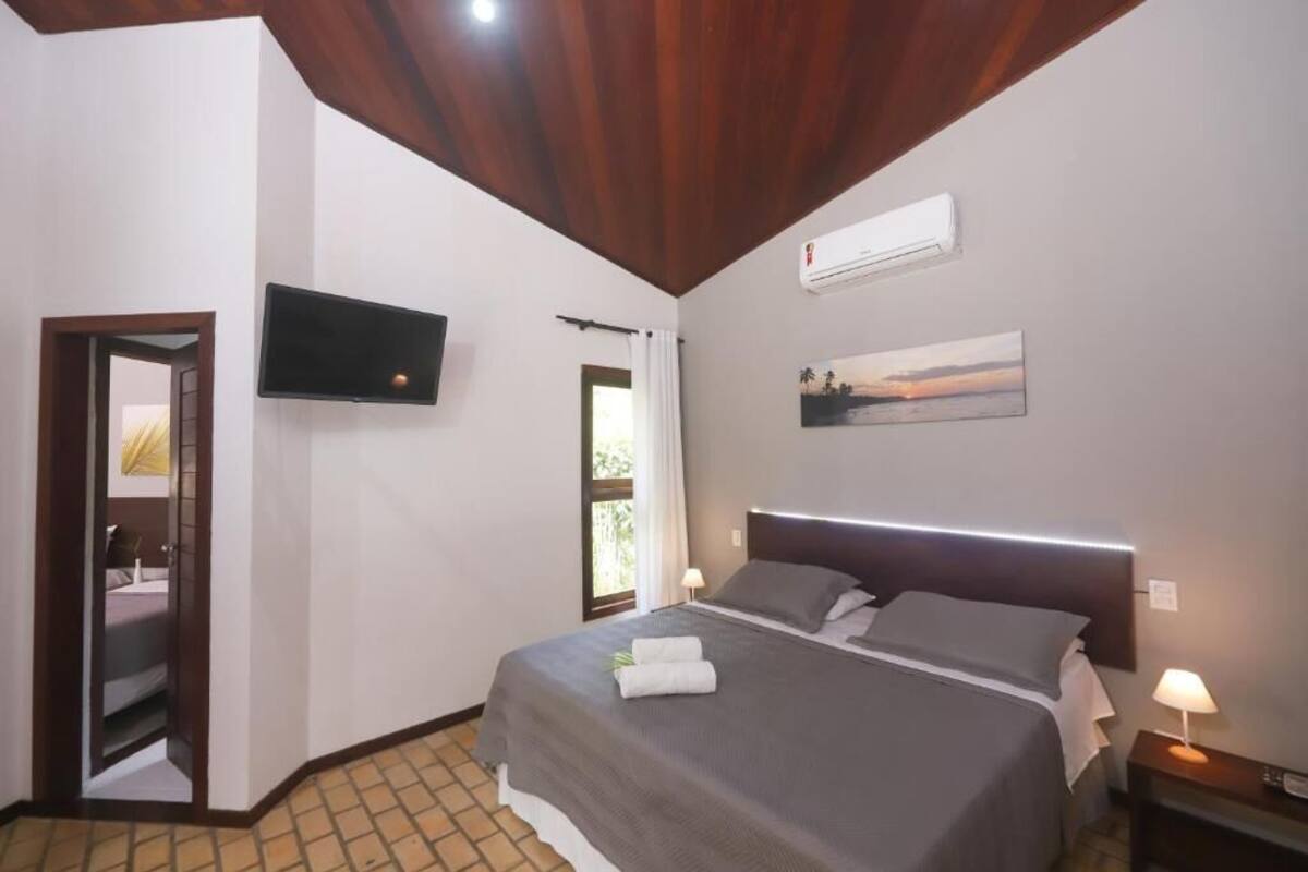 Una habitación de hotel con una cama, un televisor montado en la pared, un cuadro y un equipo de aire acondicionado.