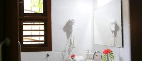 A bathroom with a white sink, a mirror, a hairdryer, and a window with blinds.