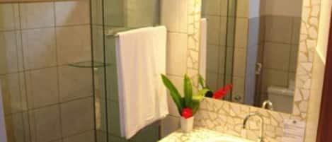 A bathroom with a glass shower enclosure, a white sink with a mosaic backsplash, and a mirror with a decorative frame.