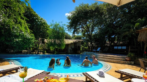 A poolside area with lounge chairs, a table with a drink and fruit, and a pool with people swimming. - Brasil Tropical Village (Tibau do Sul)