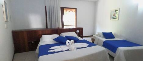 A hotel room with two beds, a wooden headboard, a ceiling fan, a window with curtains, and a small bedside table with a lamp.