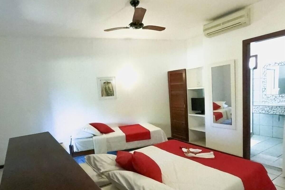 Habitación de hotel con dos camas, un escritorio, ventilador de techo, televisor y balcón con pared de piedra.