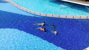 Swimmers enjoy the pool's tiled bottom surrounded by lounge chairs and umbrellas.