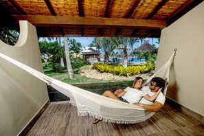 A hammock on a wooden deck with a view of a pool and palm trees. - Cana Brava All Inclusive Resort (Ilhéus)