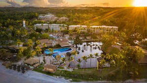 Vista aérea de un resort con varias edificaciones, una piscina y palmeras circundantes.