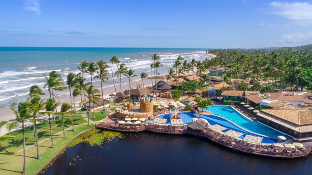 Un resort con una gran piscina, acceso a la playa y palmeras.