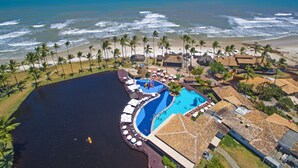 Vista aérea de un complejo turístico con piscina, playa y palmeras.