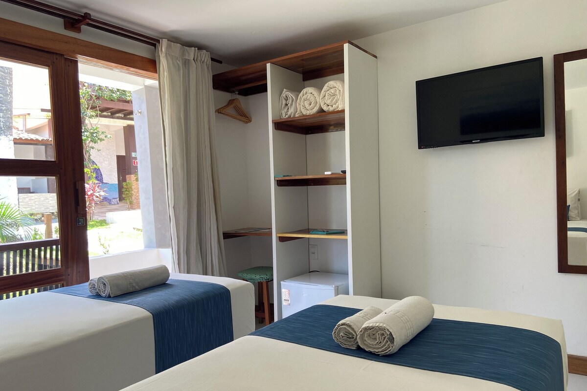Habitación de hotel con dos camas, televisión y balcón con vistas.