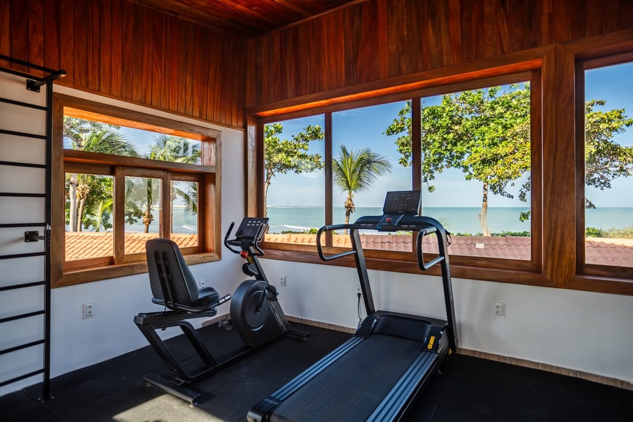 Un gimnasio con equipo de ejercicio y grandes ventanales con vista a la playa.