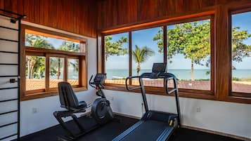 Un gimnasio con equipo de ejercicio y grandes ventanales con vista a la playa.