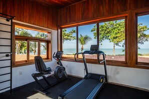 Un gimnasio con equipo de ejercicio y grandes ventanales con vista a la playa.