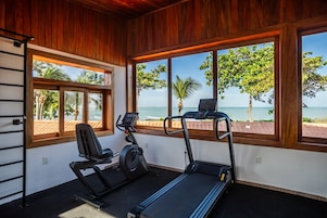 Un gimnasio con equipo de ejercicio y grandes ventanales con vista a la playa.