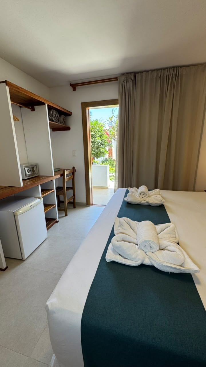 Ein Hotelzimmer mit Bett, Schreibtisch, Kühlschrank und Blick ins Freie.