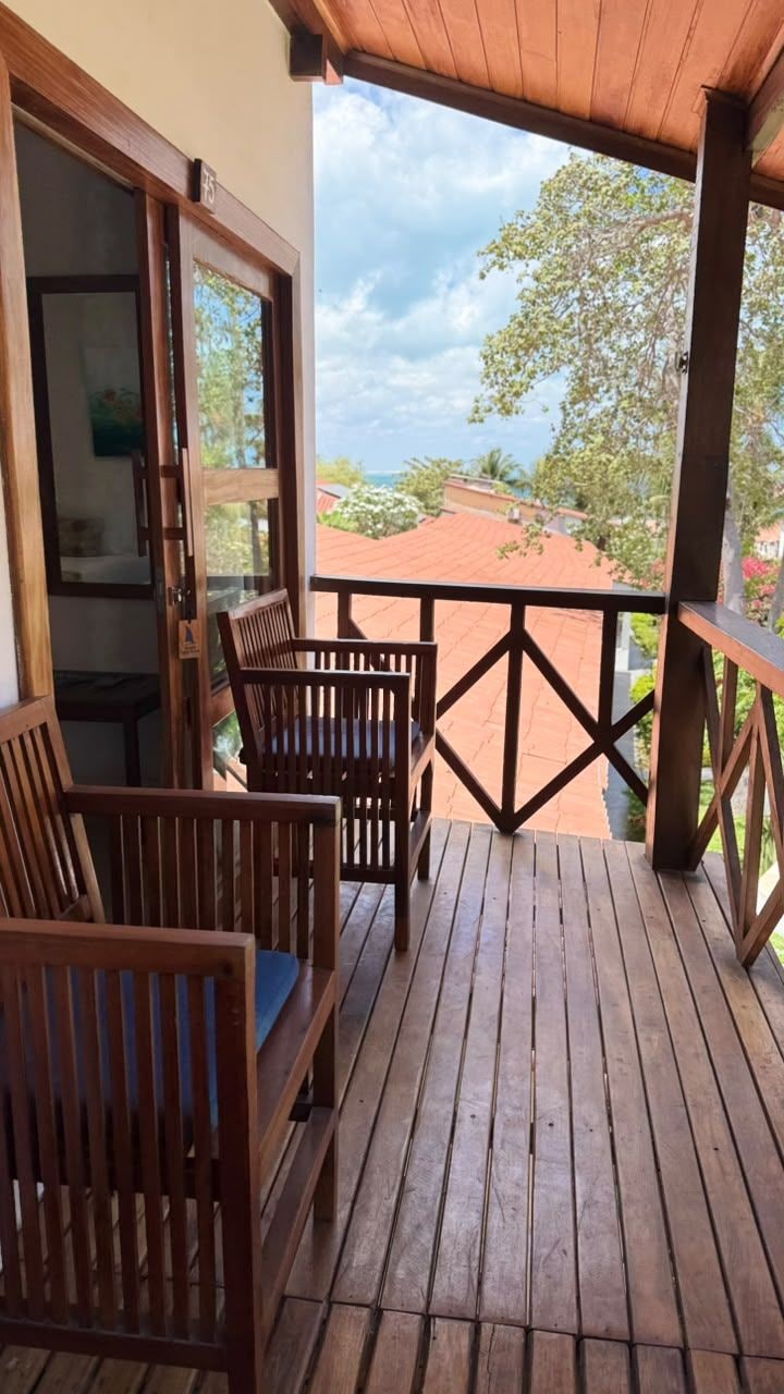 A wooden deck with two wooden chairs and a table, overlooking a red-roofed building and a clear sky.
