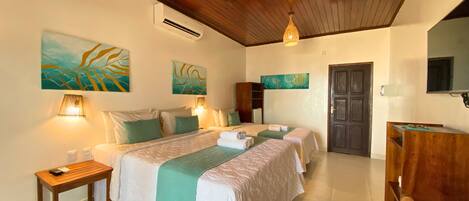Habitación de hotel con techo de madera, dos camas con ropa de cama verde y blanca, una mesita de noche de madera, una pequeña mesa y un televisor en la pared.