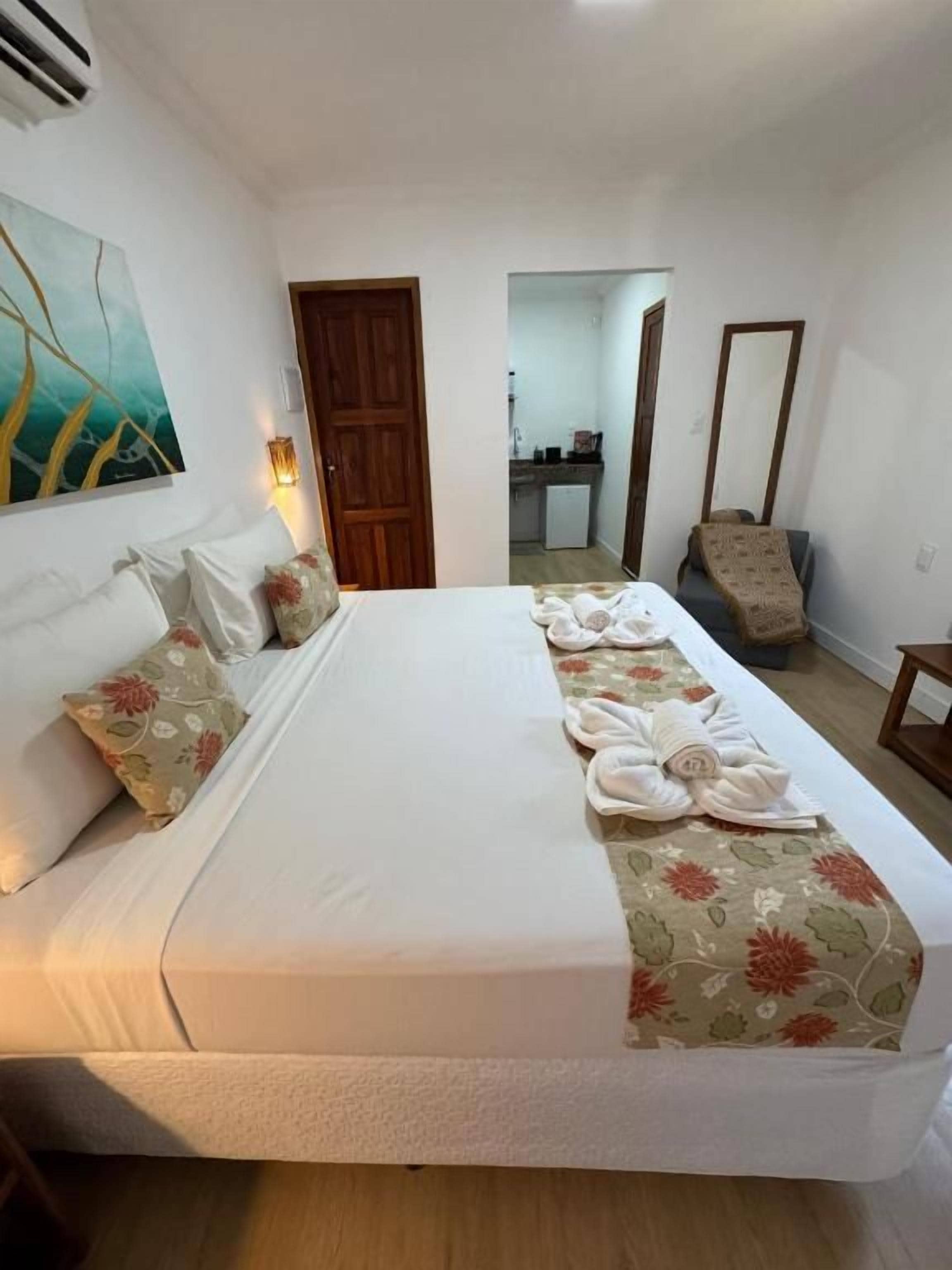 A hotel room with a large bed, a wooden door, a mirror, and a small table.