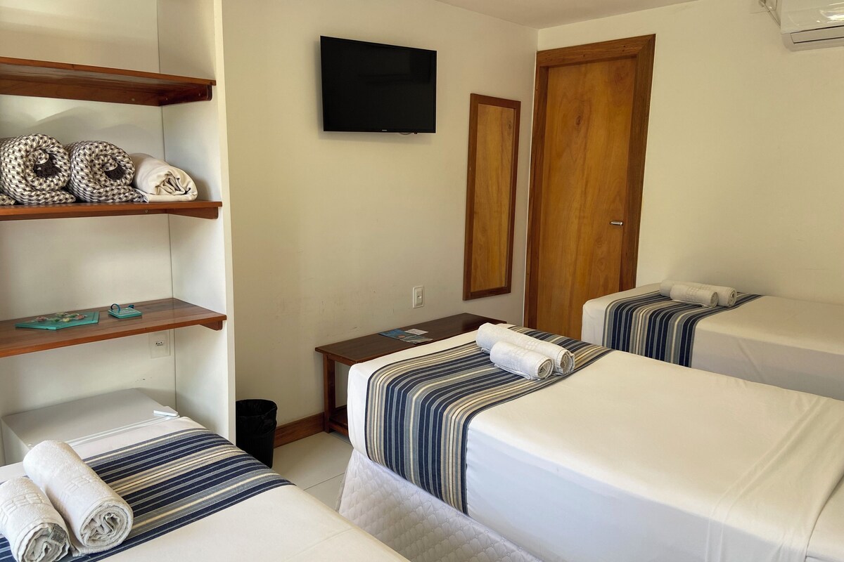 Habitación de hotel con dos camas, televisión, estanterías de madera y un cesto de basura.
