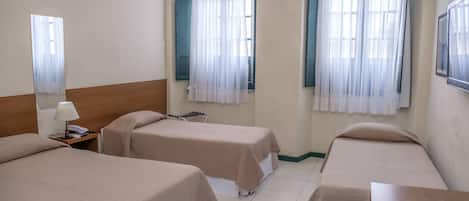 Habitación de hotel con dos camas individuales, cabecera de madera, mesita de noche con lámpara y un espejo.