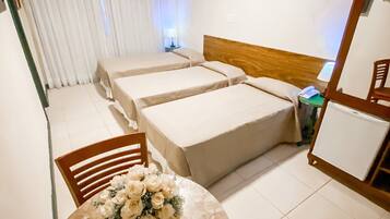 Habitación de hotel con dos camas individuales, una mesita con un jarrón de flores, una silla, un espejo y una mesita de noche con una lámpara.