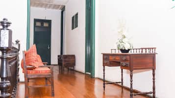 A hallway with wooden flooring, a chair with a red cushion, a wooden desk with drawers, and a green door in the background.