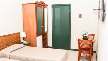 Een hotelkamer met een bed, een houten kledingkast, een groene deur, een tafeltje met een stoel en een aan de muur bevestigde televisie.