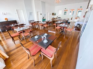 Un comedor amplio con varias mesas y sillas, suelo de madera y una lámpara moderna.