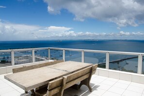 Una mesa y banco de madera en un balcón con vista al mar y a las embarcaciones.