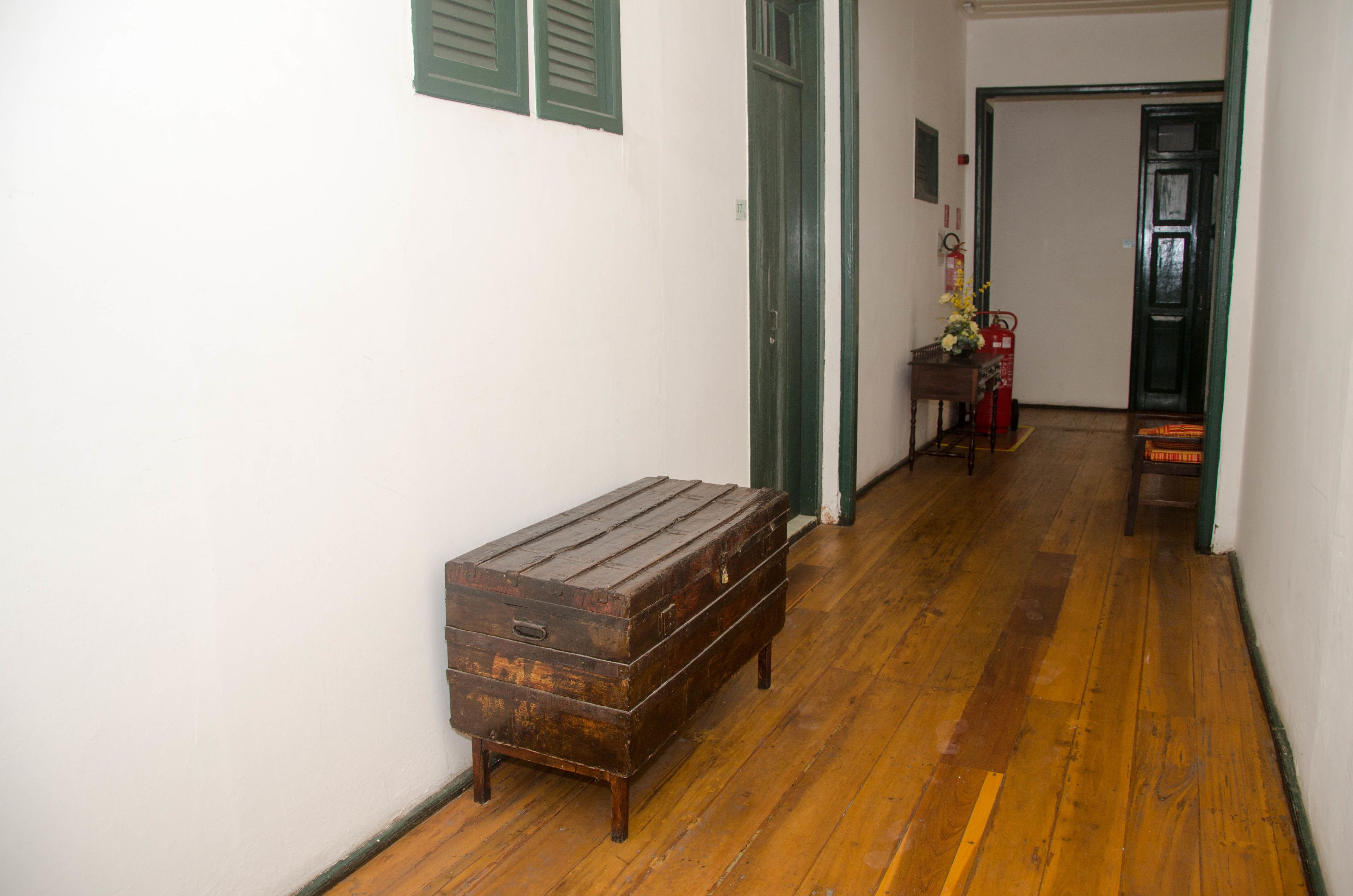 A hallway with wooden flooring, a wooden bench, a door, and a small table with a vase.