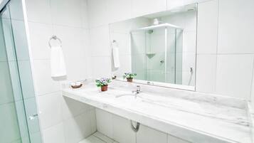 Un baño moderno con mampara de ducha de vidrio, un espejo grande y dos lavamanos.