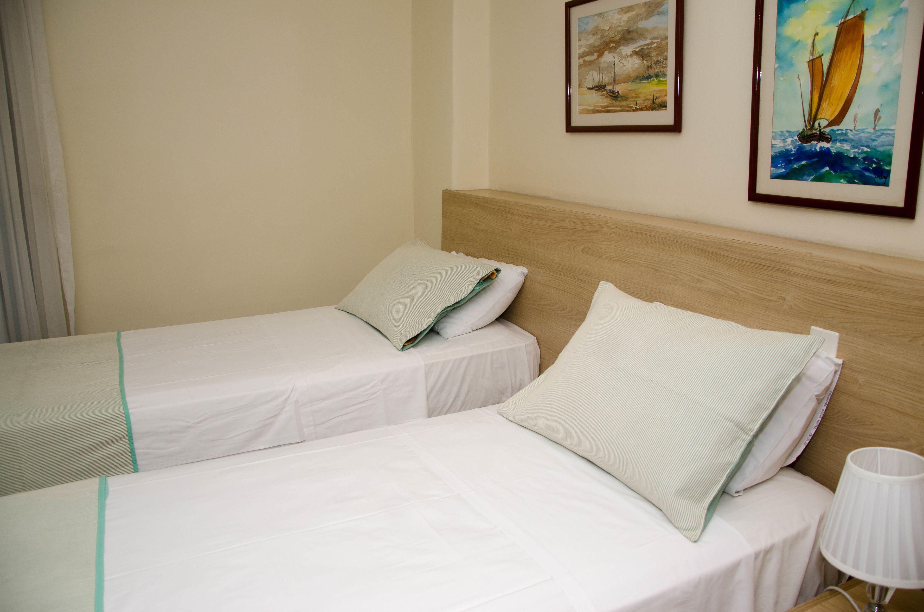 Two single beds with white linens and green trim, a wooden headboard, and a wall-mounted lamp.