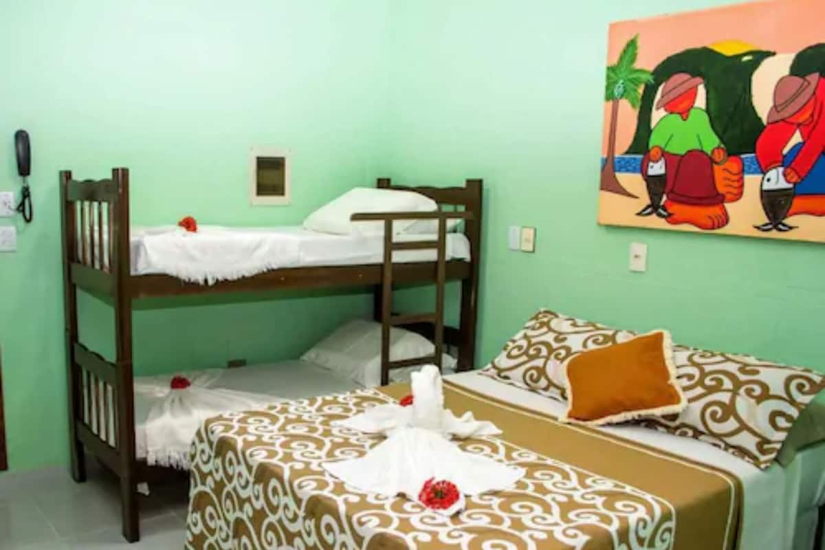 A room with bunk beds, a patterned bedspread, a painting on the wall, and a telephone.