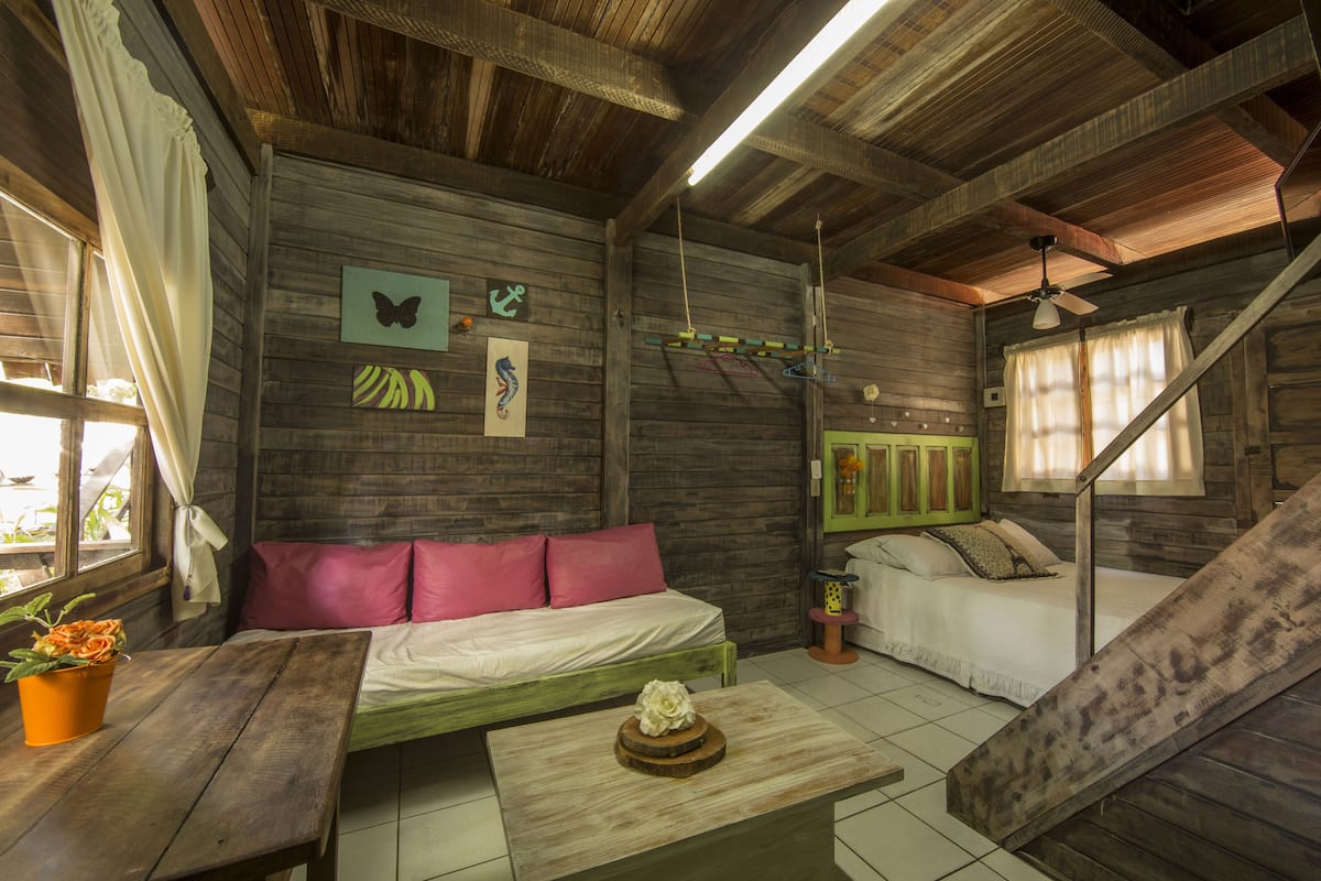 A rustic wooden room with a bed, a sofa, a small table, and a staircase.