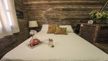 Una habitación acogedora con techo de madera, una cama con ropa blanca, una mesita de noche con lámpara y un cartel en la pared.