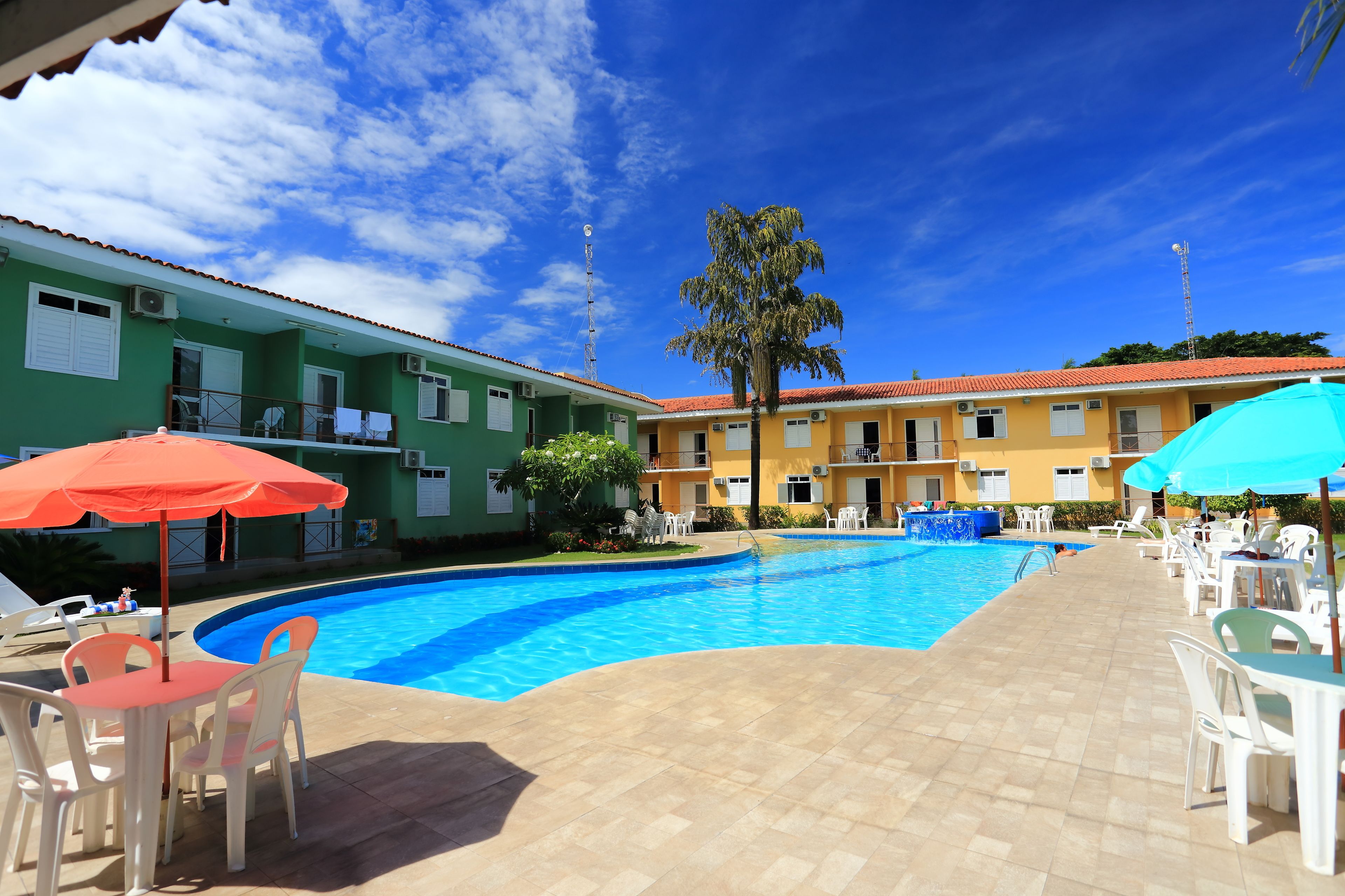 A swimming pool with lounge chairs and umbrellas, surrounded by buildings with red-tiled roofs.