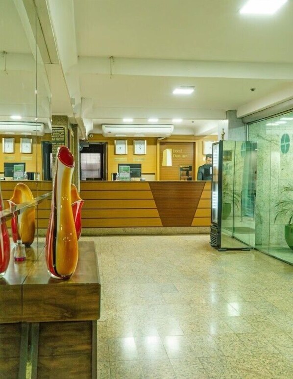 Uma área de recepção de hotel com um balcão de madeira, um relógio e uma parede de vidro.