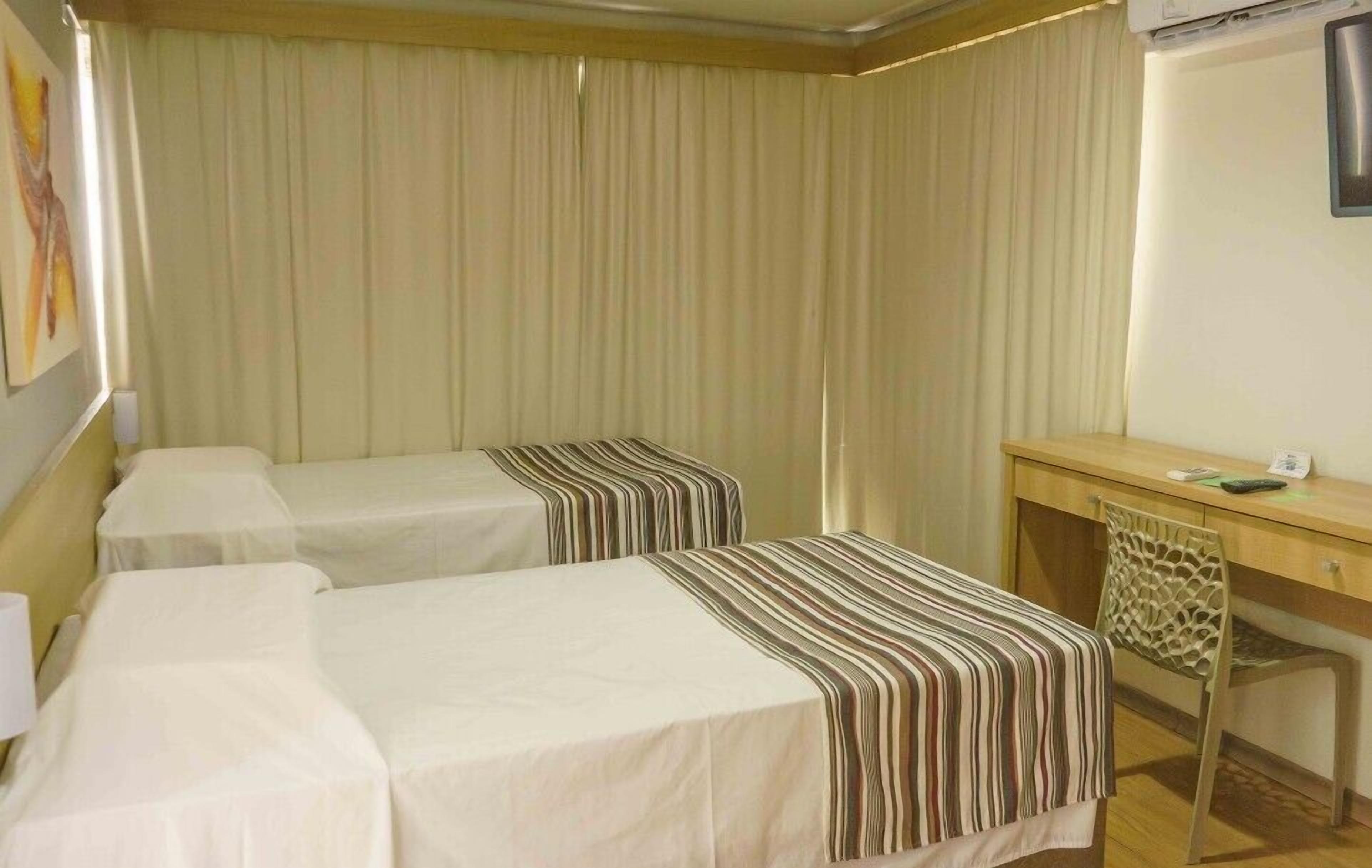 A hotel room with two single beds, a desk, and a chair.