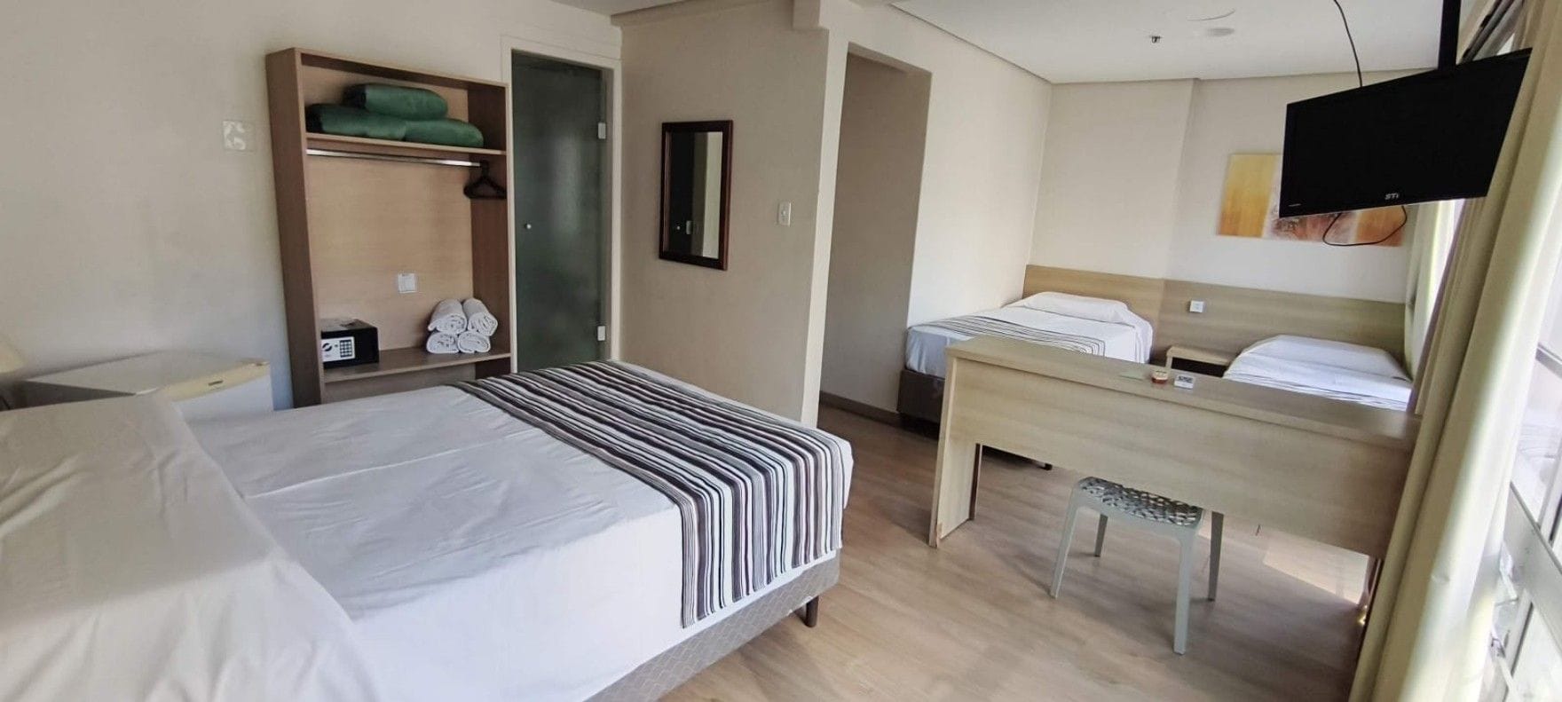 A hotel room with a bed, a desk, a mirror, and a television.