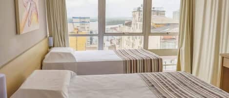 A hotel room with two beds, a window with a city view, and a painting on the wall.