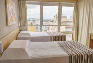 Ein Hotelzimmer mit zwei Betten, einem Fenster mit Blick auf die Stadt und einem Gemälde an der Wand.