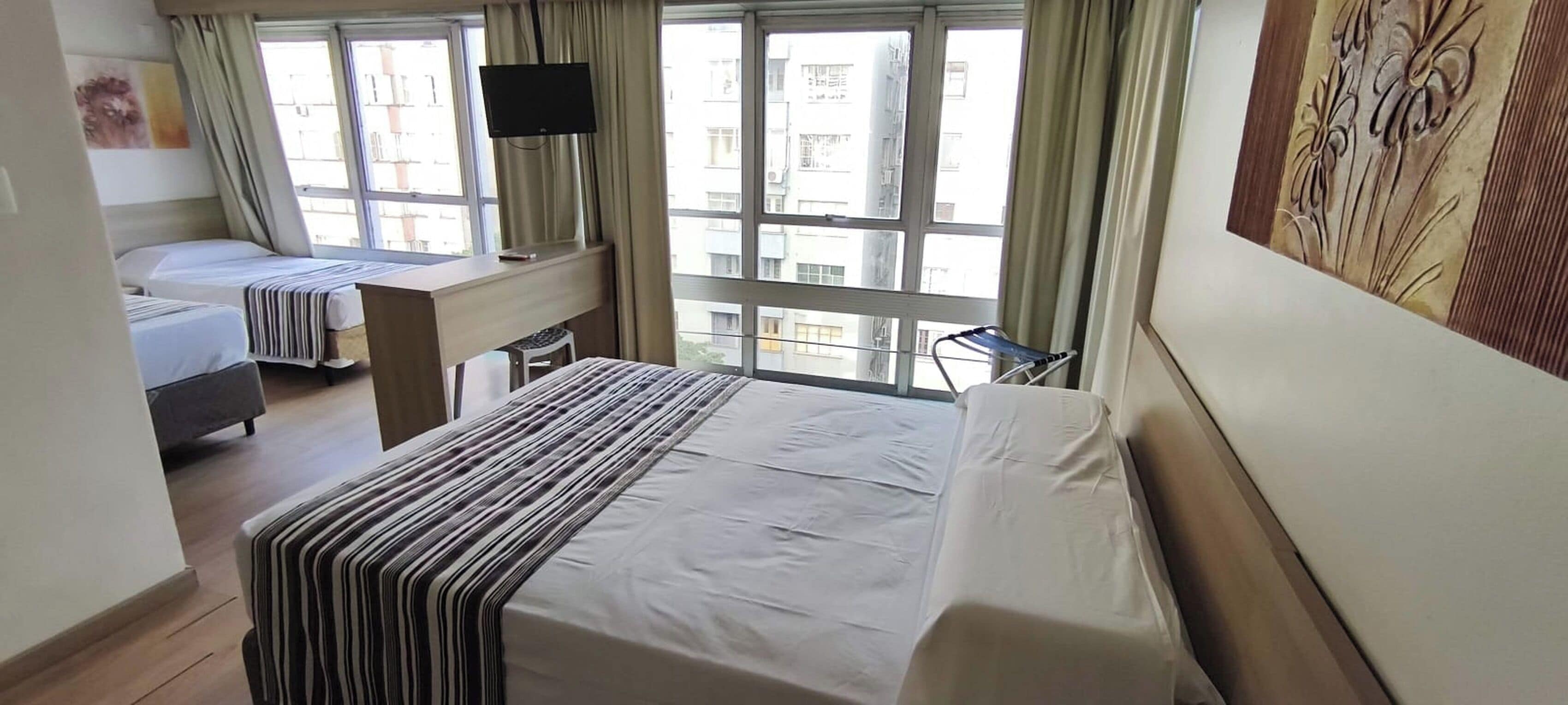 Habitación de hotel con dos camas, un escritorio, una silla, un televisor y una ventana con cortinas.