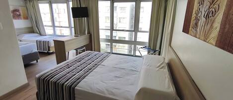 Habitación de hotel con dos camas, un escritorio, una silla, un televisor y una ventana con cortinas.